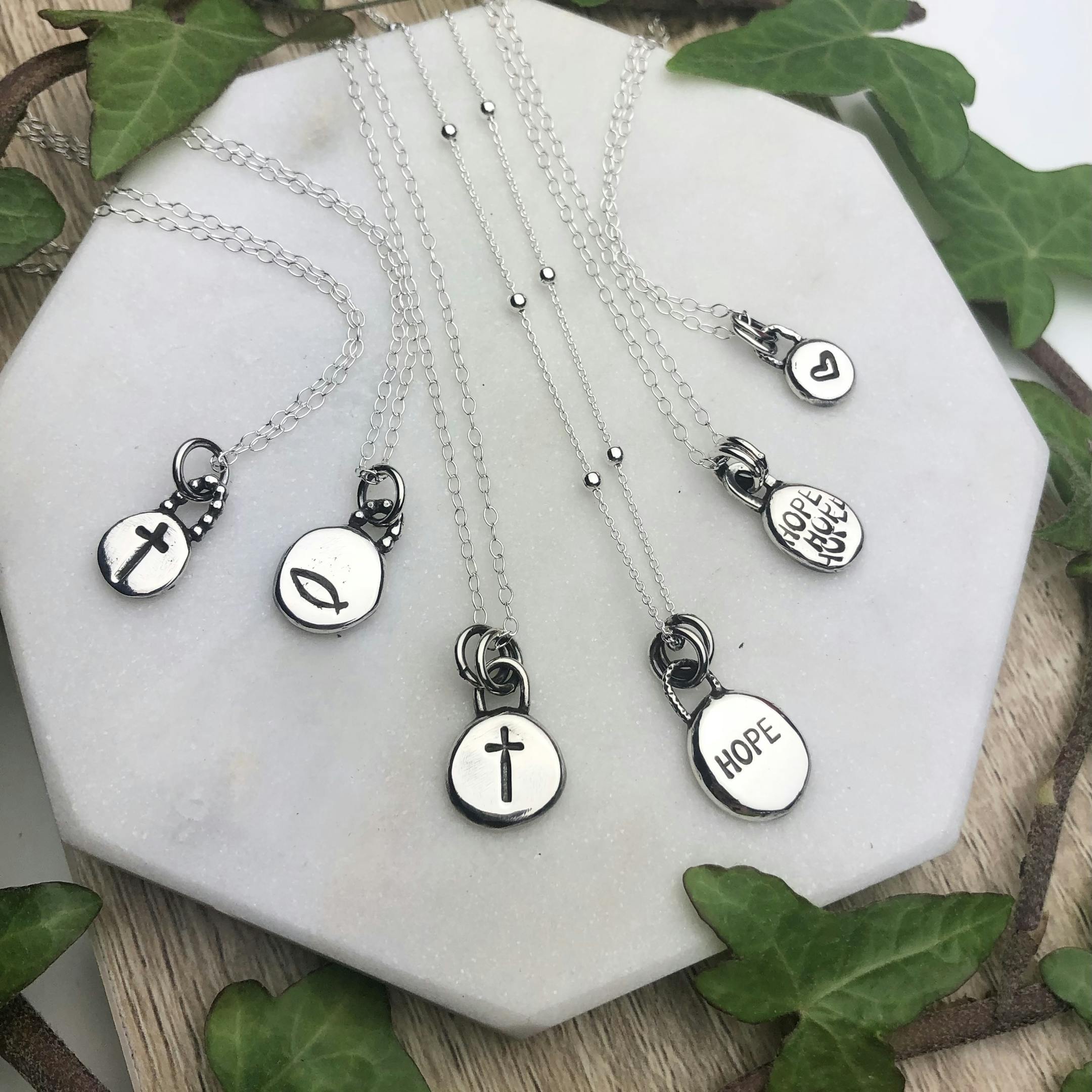 Flatlay of six silver pebble Christian necklaces with cross, fish and hope | Bloom Jewellery @ Cheerfully Given