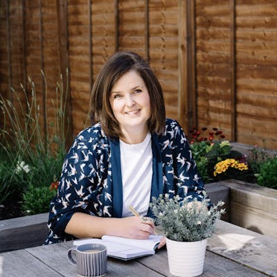 Cath Sales sitting at table outside writing of Hope and Ginger at Cheerfully Given